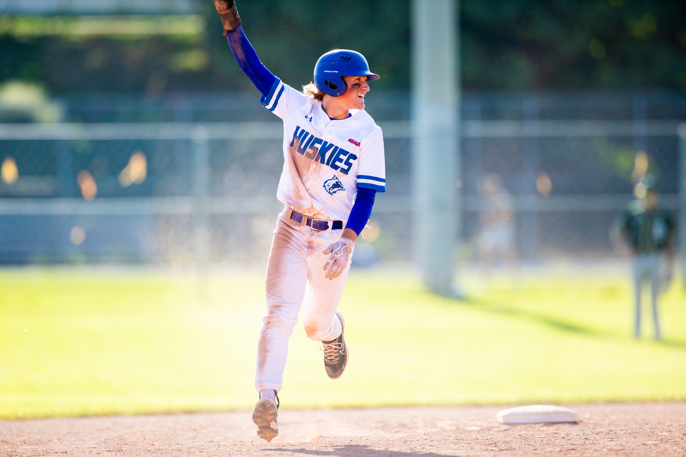 Huskies baseball player runs around base with hand in the air celebrating.
