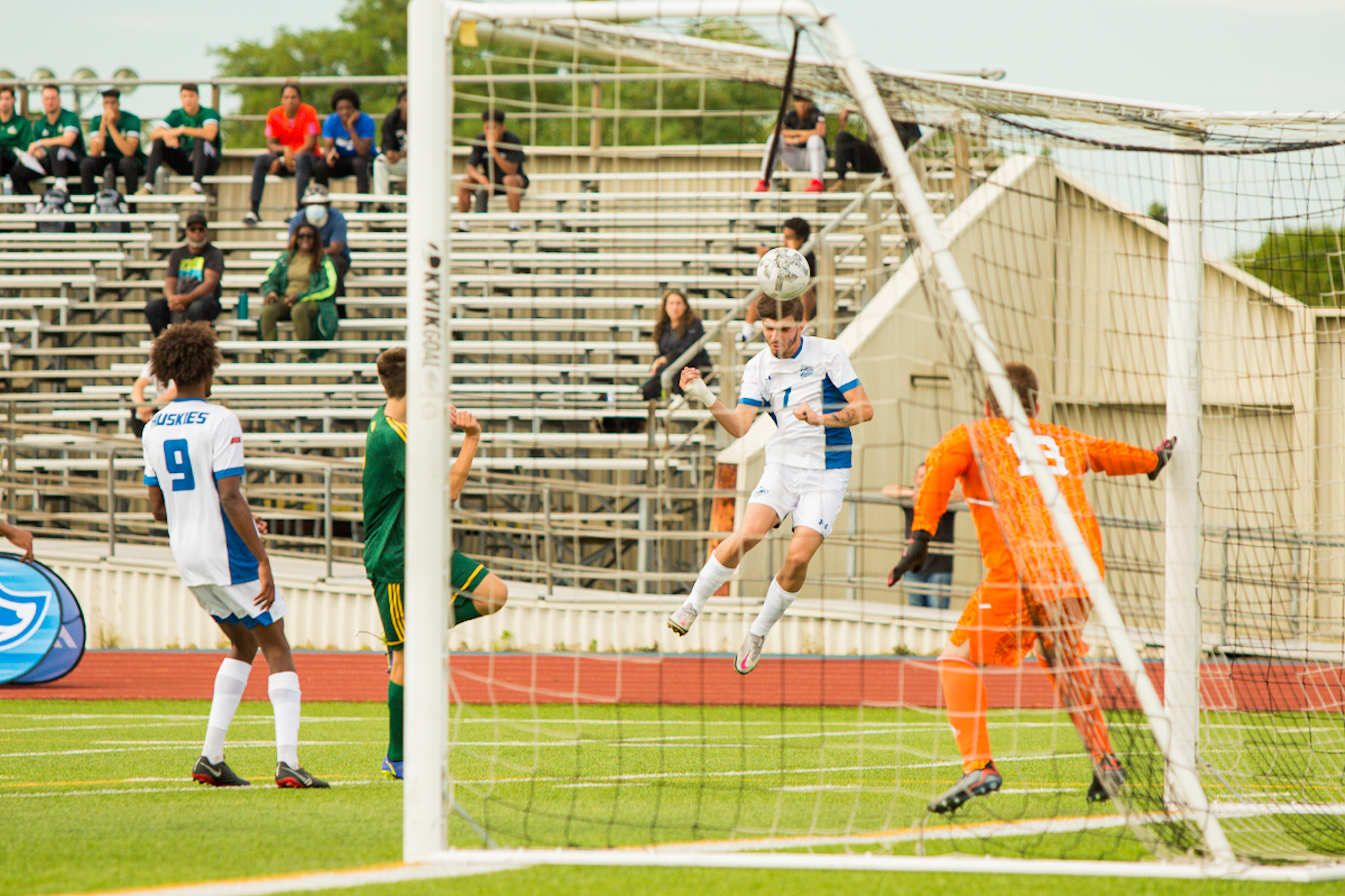 Men's soccer player heads ball towards goalie