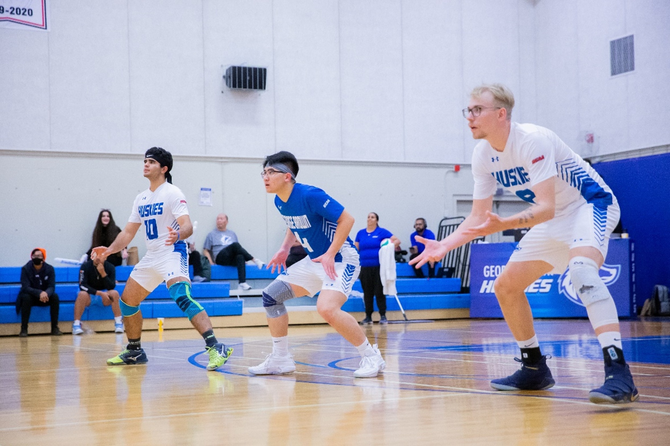 Three Huskies volleyball players wait for serve in defensive position