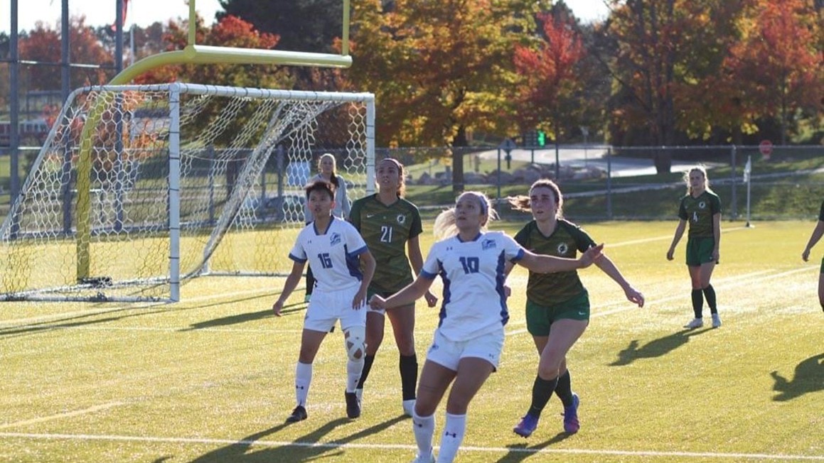 Four soccer players look up as ball comes down